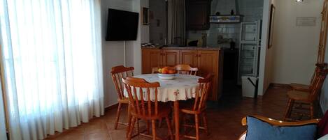 Un comedor con una mesa redonda y sillas, una cocina al fondo y una sala de estar con sofá.