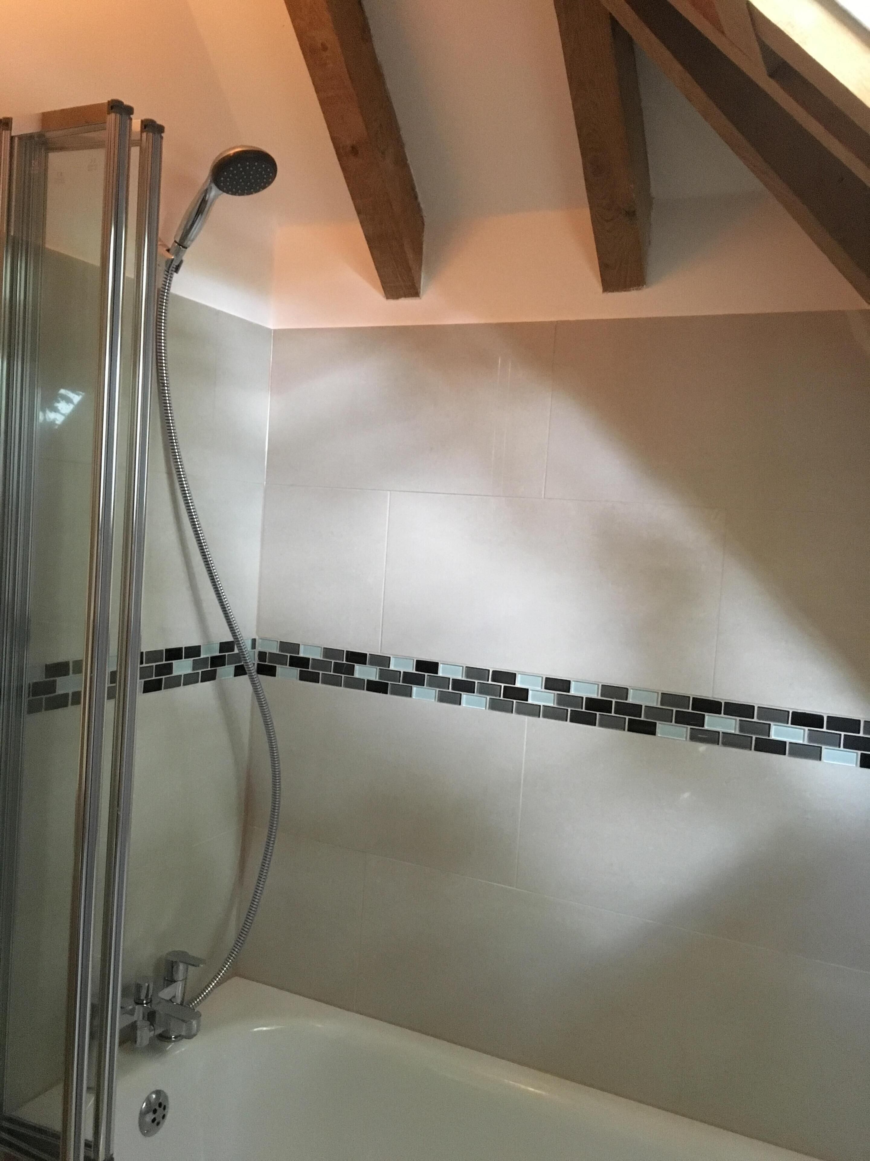 A shower with a glass enclosure, a handheld showerhead, and a tiled wall with a mosaic border.