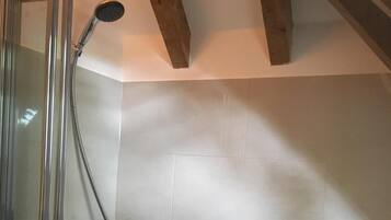 A shower with a glass enclosure, a handheld showerhead, and a tiled wall with a mosaic border.