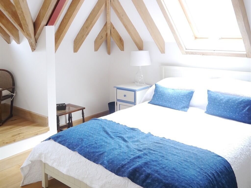 A bedroom with a large bed, a nightstand, a chair, and a skylight.