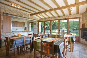 A spacious dining area with wooden tables and chairs, stone walls, and large windows offering a view of the outdoors. - Legaire Etxea (Asparrena)