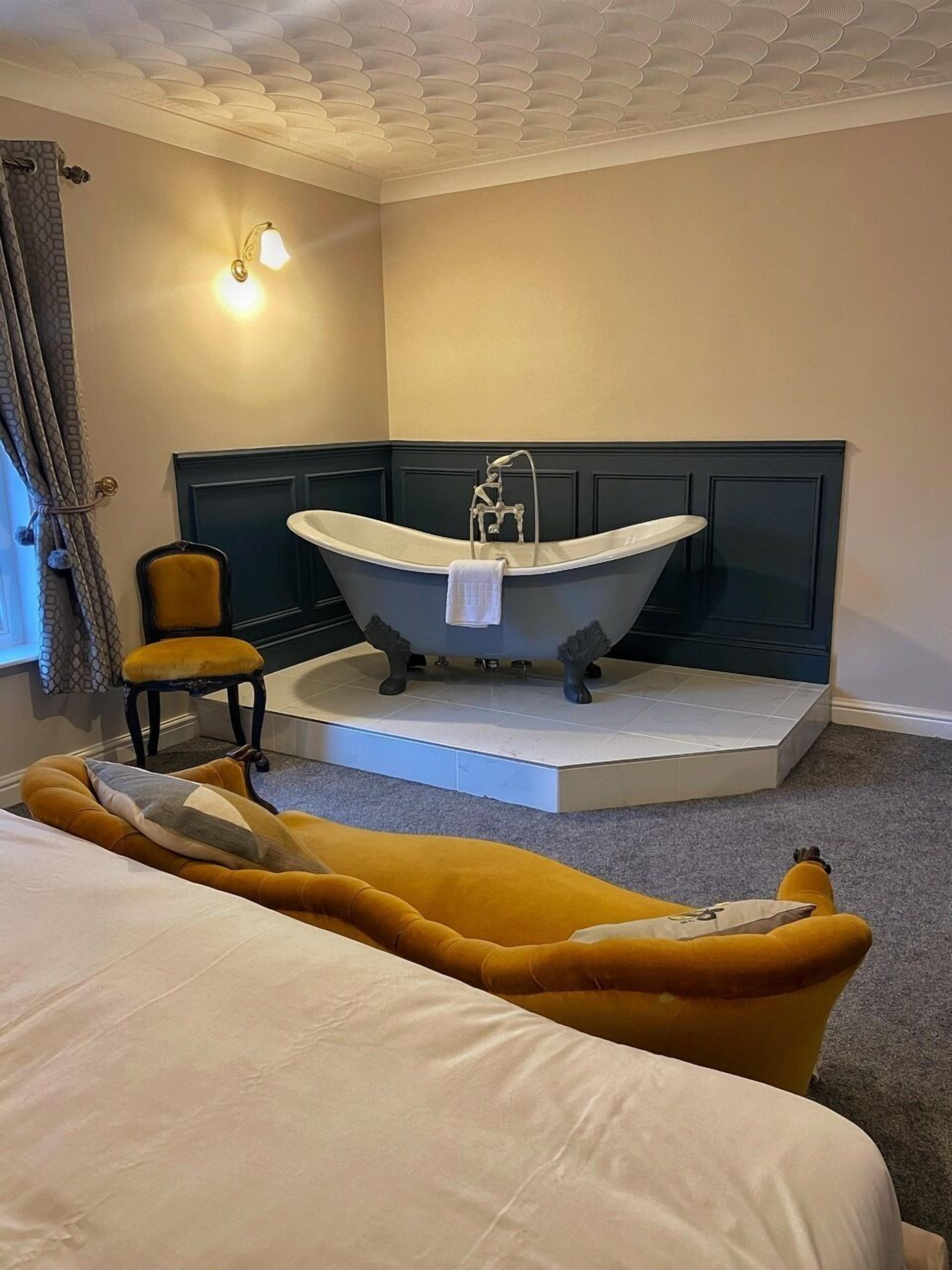 A room with a bathtub, a chair, and a bed.