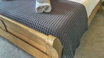 A neatly made bed with a grey textured bedspread and pillows, a wooden headboard, and a small bedside table with a lamp.