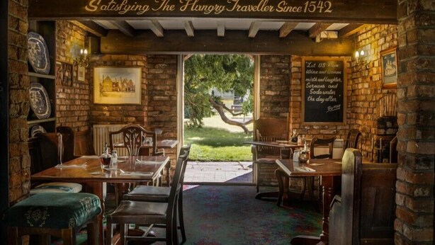 A rustic pub interior with brick walls, wooden furniture, and a view of the outdoors. - The Leagate Inn (Boston)