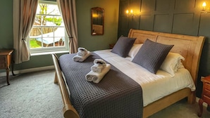 A bedroom with a large bed, a wooden headboard, a window with curtains, a bedside table, and a wall-mounted light fixture. - The Leagate Inn (Boston)