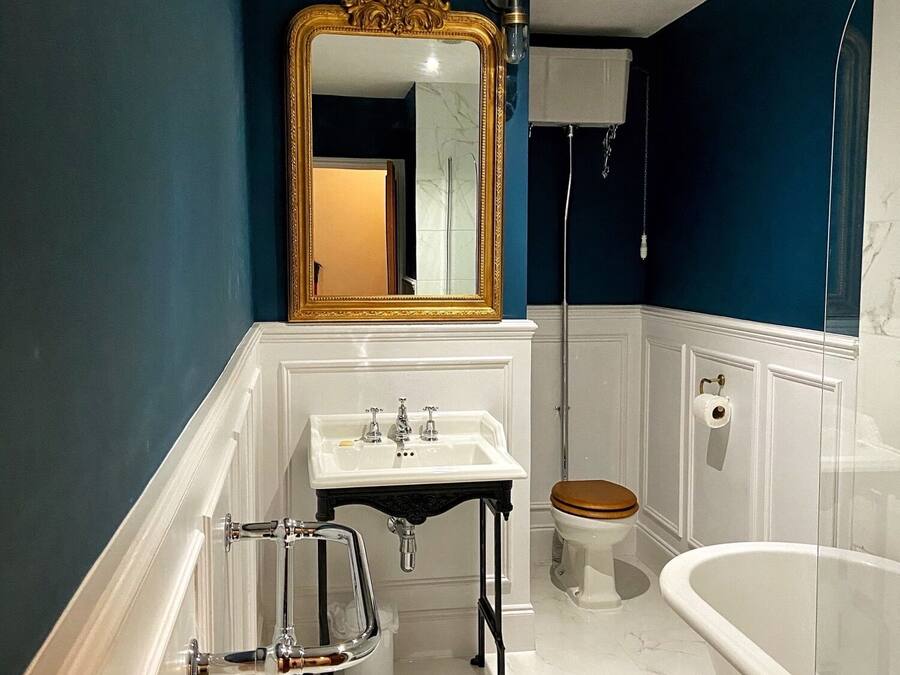 A bathroom with a white sink, a freestanding bathtub, a toilet, and a large mirror with a gold frame.