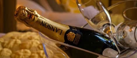 A bottle of Lanson champagne in a glass container with ice cubes, surrounded by empty champagne glasses on a table.