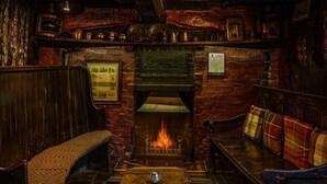 A cozy pub interior with a fireplace, wooden benches, and a small table. - The Leagate Inn (Boston)