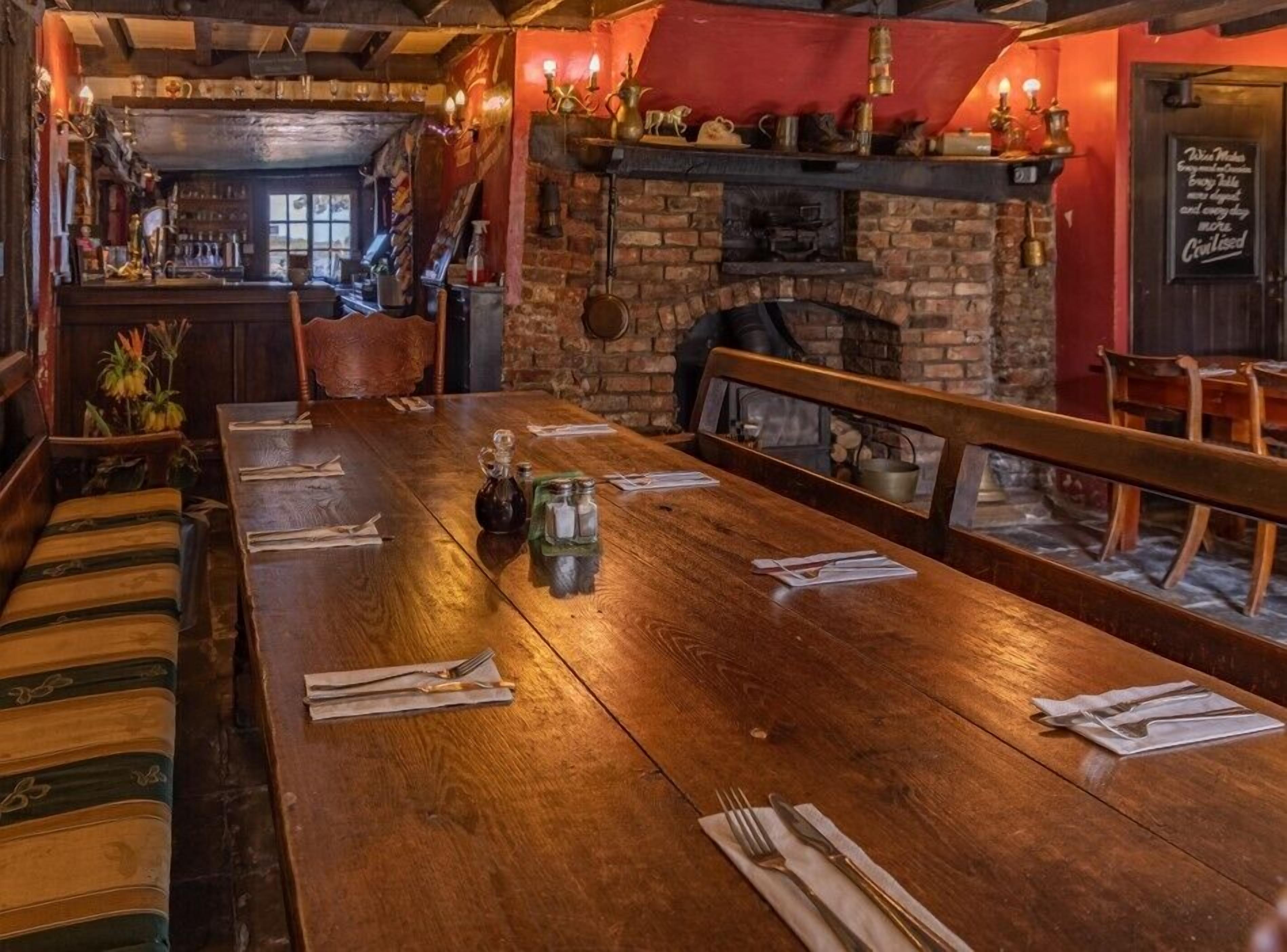 A long wooden table set for dining, with a brick fireplace and decorative items on the mantel.
