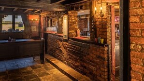 A rustic bar area with a stone wall, wooden counter, and a view of the outside. - The Leagate Inn (Boston)