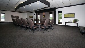 A conference room with a large table surrounded by chairs, a black console table with a plant, and framed pictures on the walls. - Hôtel Le Hauterive (Baie Comeau)