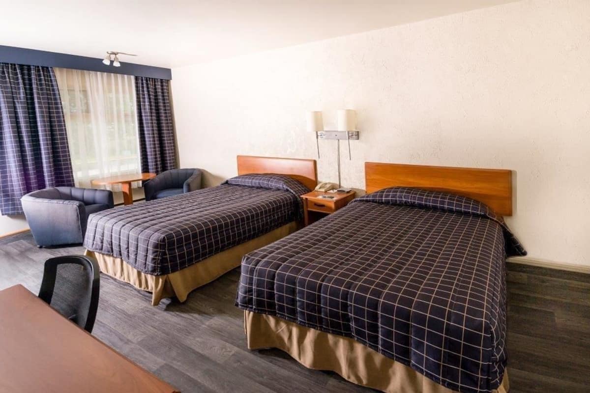 Ein Hotelzimmer mit zwei Betten, einem Schreibtisch, einem Stuhl und einem fenster mit Vorhängen.