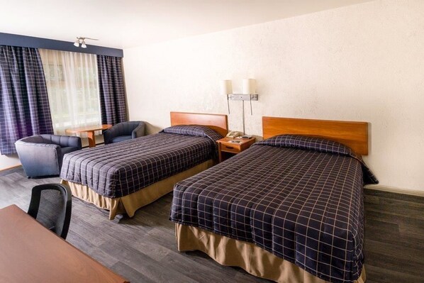 Habitació d'hotel amb dos llits, una escriptori, una cadira i una finestra amb cortines.