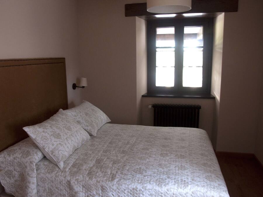 Un dormitorio con cama, mesita de noche, lámpara de pared y ventana con persianas.