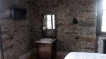 A bathroom with a stone wall, a wooden cabinet with a sink, a mirror, and a television mounted on the wall.