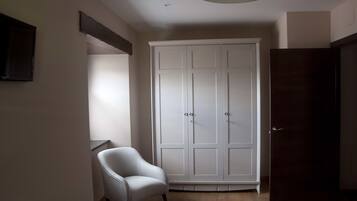 Ein Zimmer mit einem weißen Kleiderschrank, einer dunklen Tür und einem weißen Sessel.