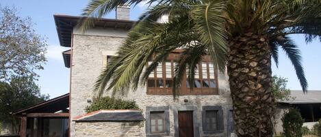 Un edificio de piedra con un patio cubierto, una palmera y un césped bien cuidado.