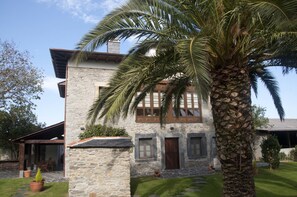 Un edificio de piedra con un patio cubierto, una palmera y un césped bien cuidado.