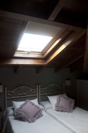 Un dormitorio con tragaluz, una cama con ropa de cama blanca y dos almohadas, y cabecero blanco.