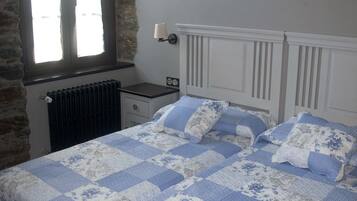 A bedroom with a double bed, a nightstand, a lamp, a window with curtains, and a radiator.