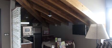 Una cocina con microondas, horno y refrigerador. Hay una mesa de comedor con sillas y una lámpara.