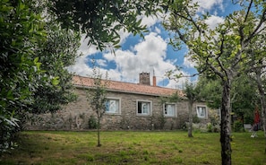 A stone building with a tiled roof, surrounded by greenery and trees.
