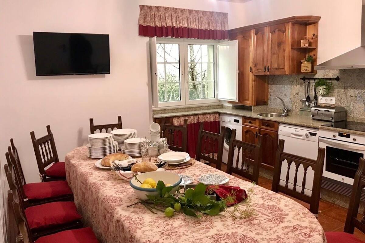 A dining area with a table set for a meal, surrounded by wooden chairs. A television is mounted on the wall above the table.