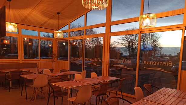 An indoor dining area with tables and chairs, large windows, and hanging lights.