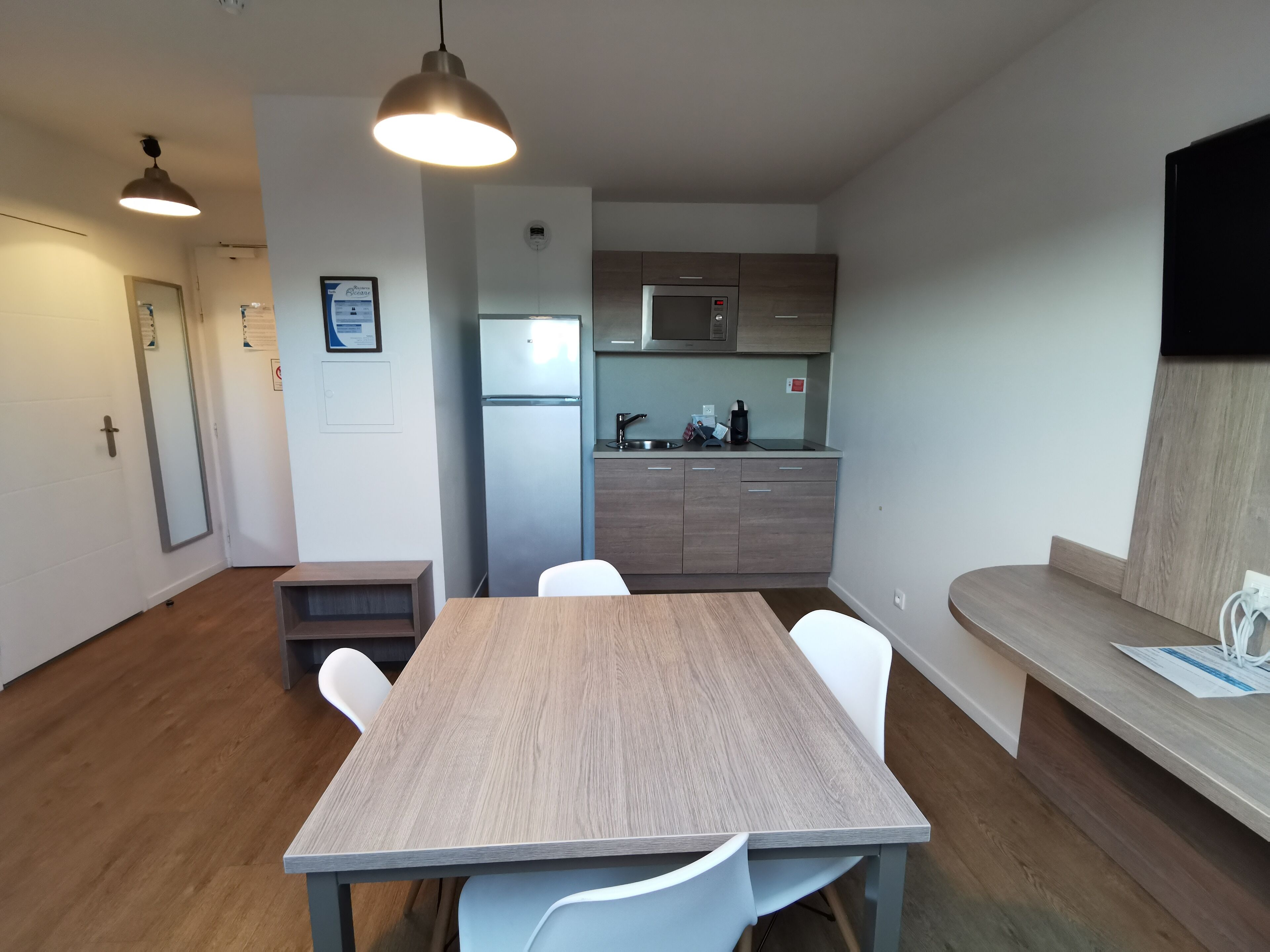 Eine moderne Küche mit integriertem Mikrowellenherd, Kühlschrank und Spüle. Ein Holztisch mit Stühlen steht bereit.
