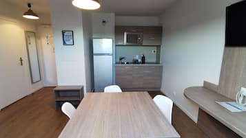 Eine moderne Küche mit integriertem Mikrowellenherd, Kühlschrank und Spüle. Ein Holztisch mit Stühlen steht bereit.