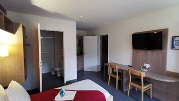 Quarto de hotel com cama, escrivaninha, televisão e armário.