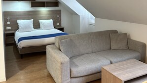 A modern room with a bed, a grey sofa, and a wooden coffee table.