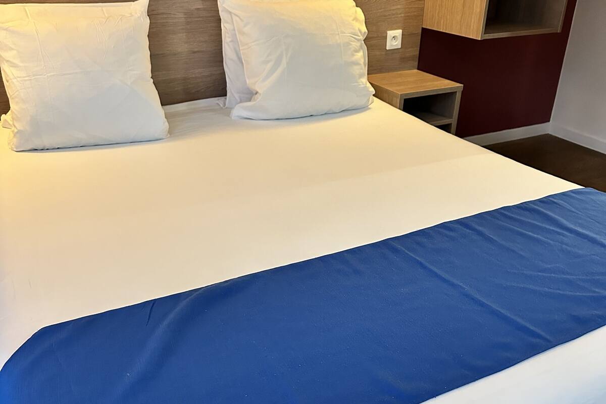 A neatly made bed with white and blue bedding, a wooden headboard, and a nightstand with a lamp.