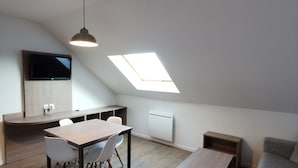 A modern loft apartment with a dining area, a sofa, a TV, and a skylight.