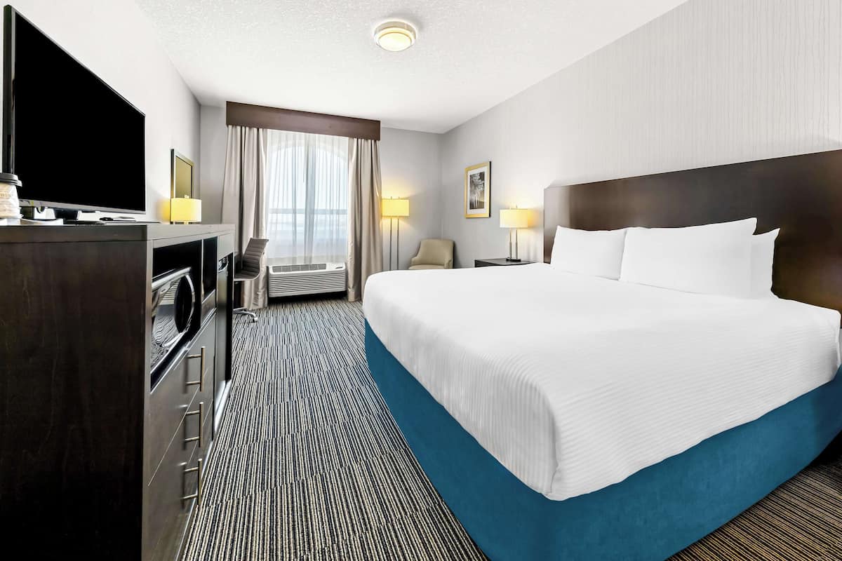 A hotel room with a large bed, a TV, a desk, and a chair.