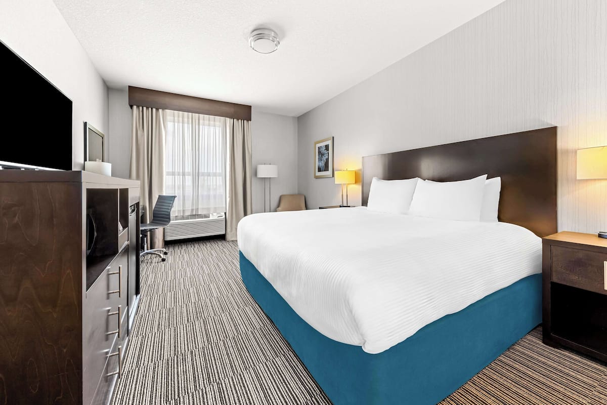 A hotel room with a large bed, a desk with a chair, a television, and a window with curtains.