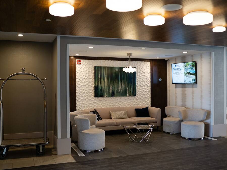 A modern lobby with a sofa, ottomans, a cart, and a wall-mounted screen.