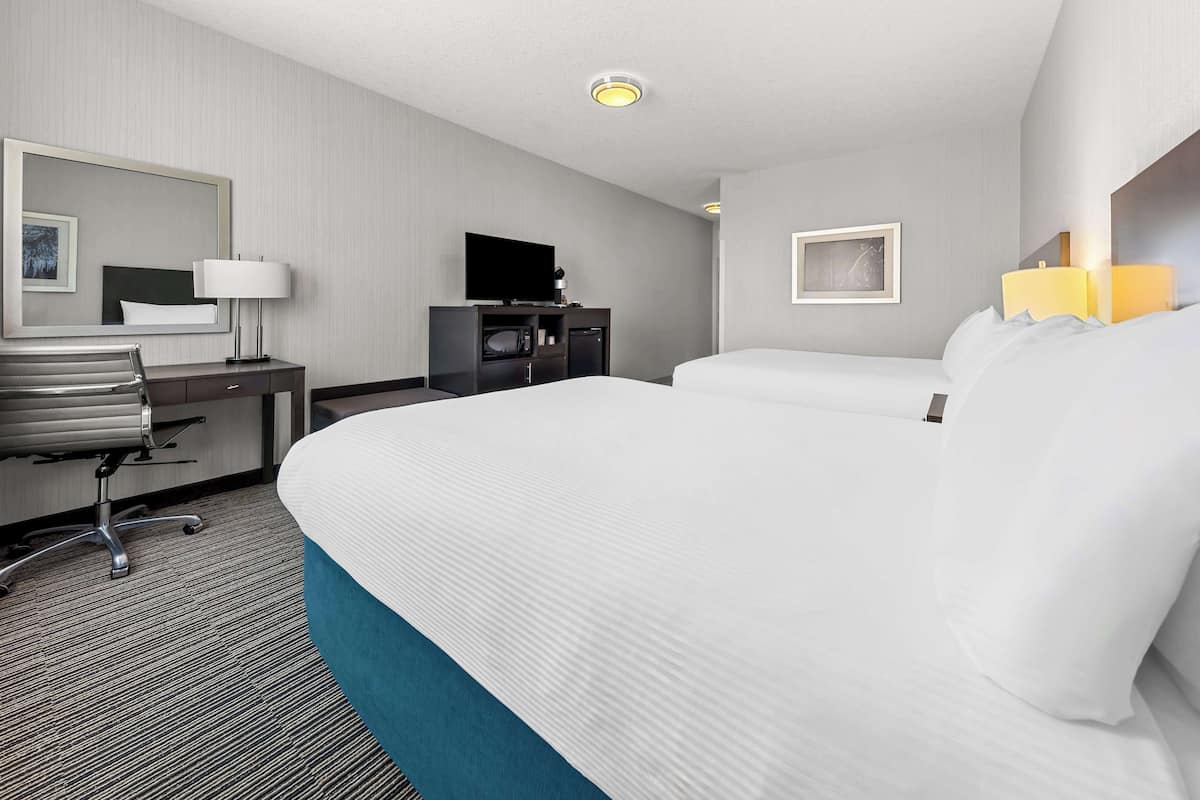 A hotel room with a large bed, a desk with a chair, a television, and a small cabinet.