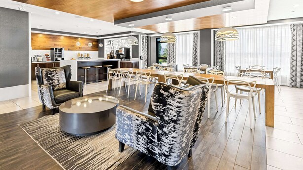 Un salon moderne avec un coin repas, comprenant une cuisine en arrière-plan, un plafond en bois et des meubles contemporains.