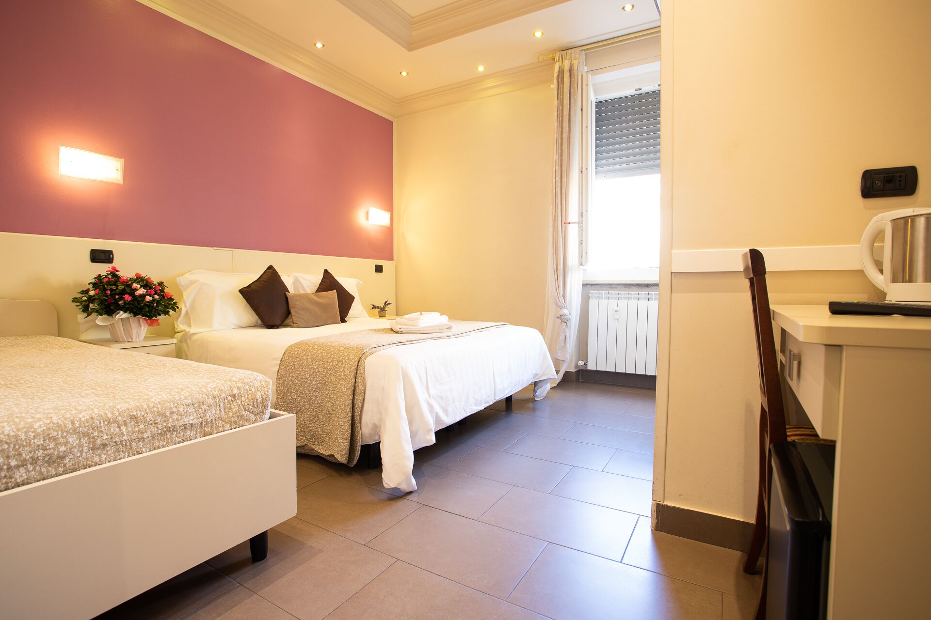 A hotel room with two beds, a kitchenette, and a bathroom visible through a window.