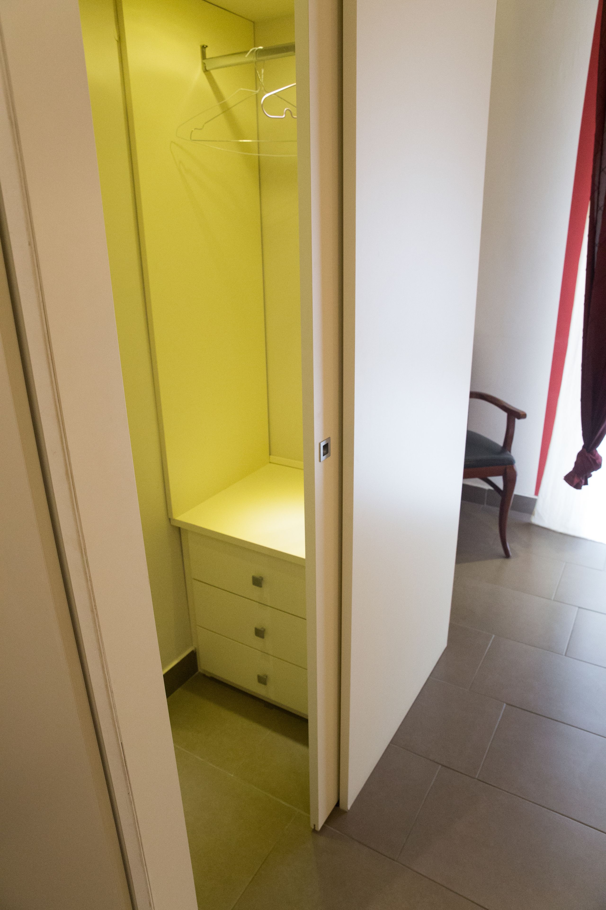 A narrow hallway with a yellow closet, a wooden chair, and a red curtain.
