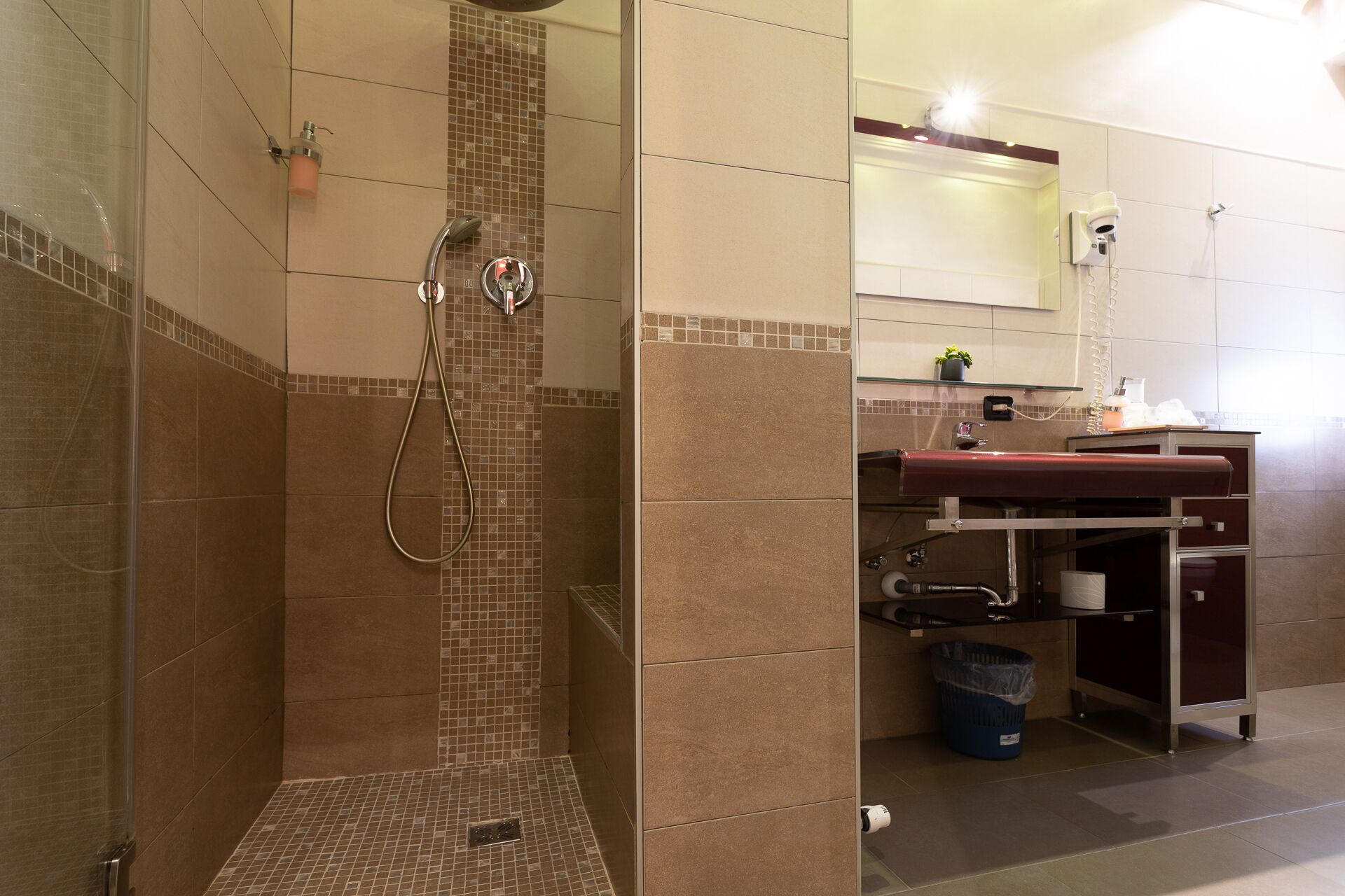 A bathroom with a shower, a sink, a mirror, and a trash bin.