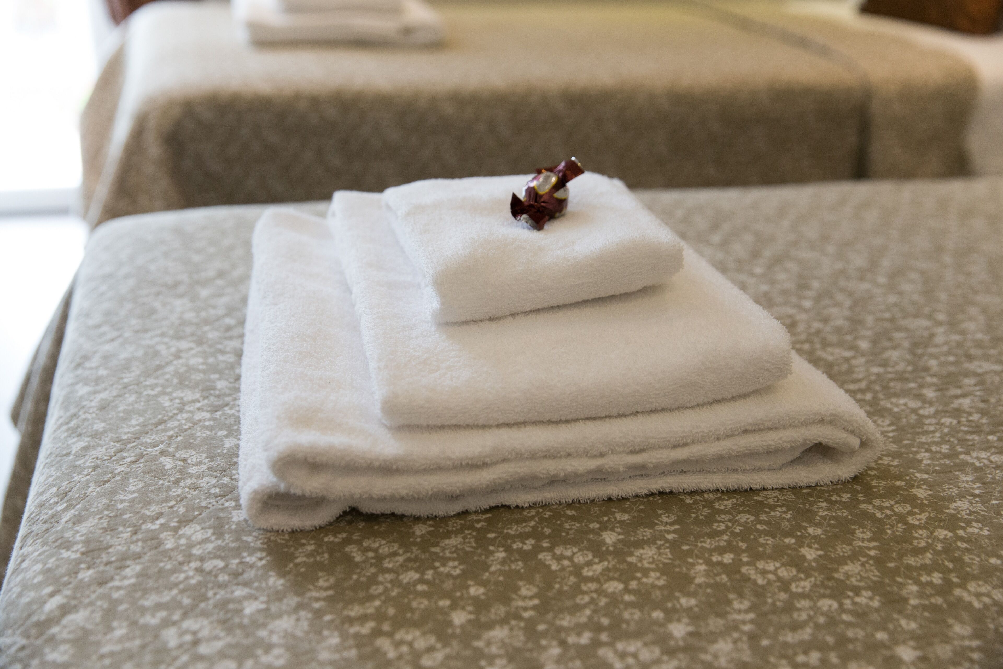 Una toalla blanca doblada cuidadosamente sobre una cama con edredón estampado con motivos florales.