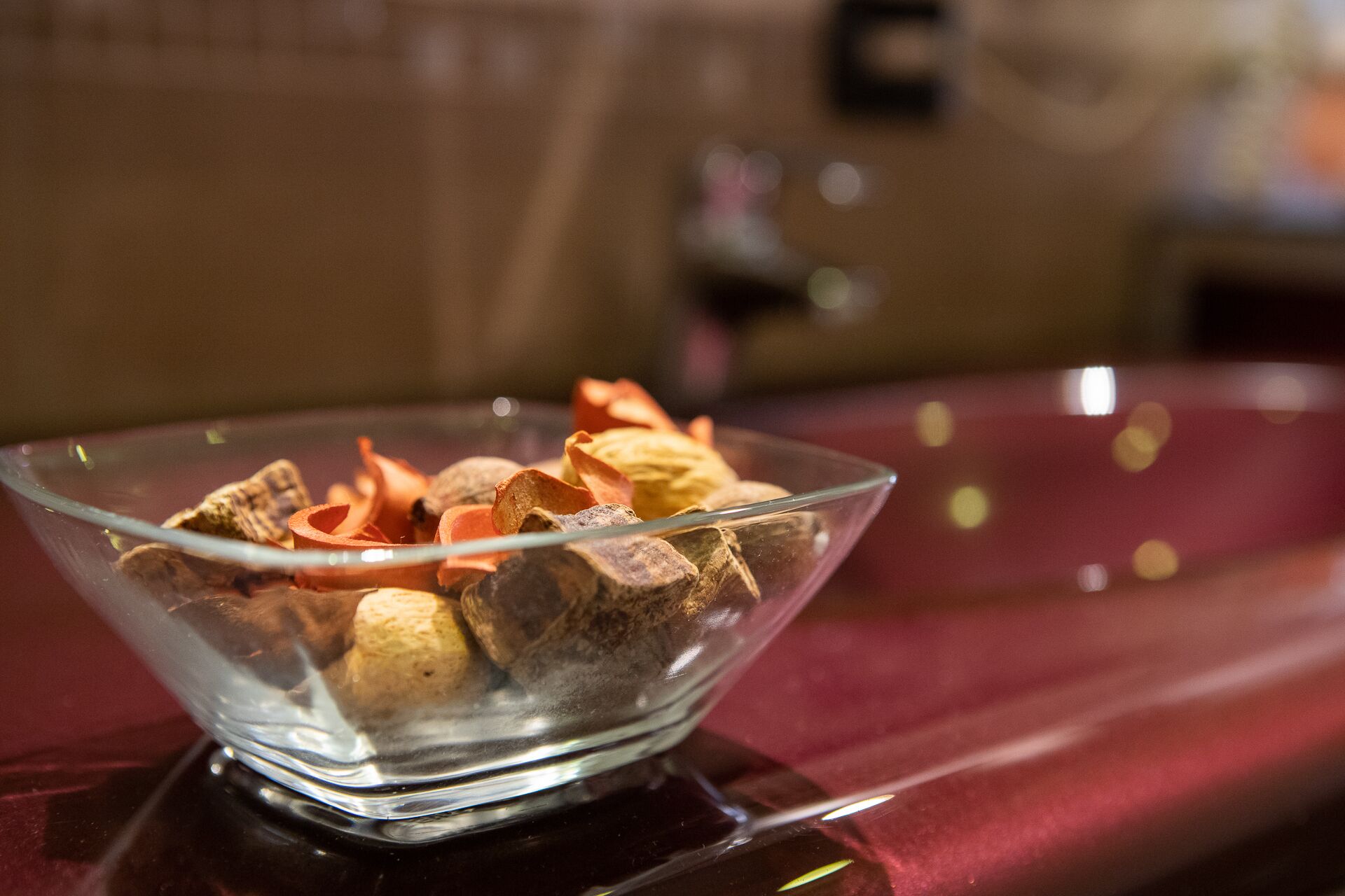A clear glass bowl containing assorted nuts and dried fruits on a reflective surface.