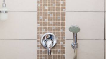 A shower area with a tiled wall, a handheld showerhead, and a wall-mounted faucet.