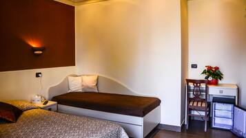 A hotel room with a bed, a desk, a chair, and a small refrigerator.