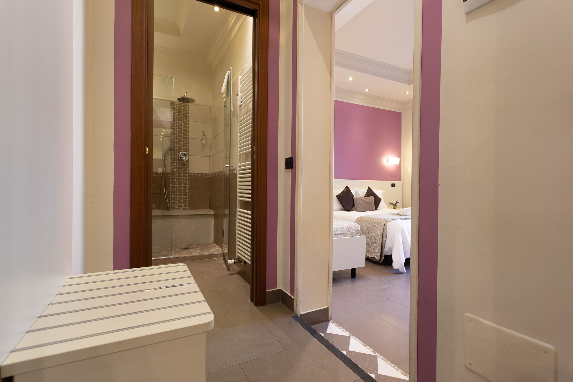 A hotel room with a bed, a bedside table, a shower area, and a bathroom with a sink and mirror.