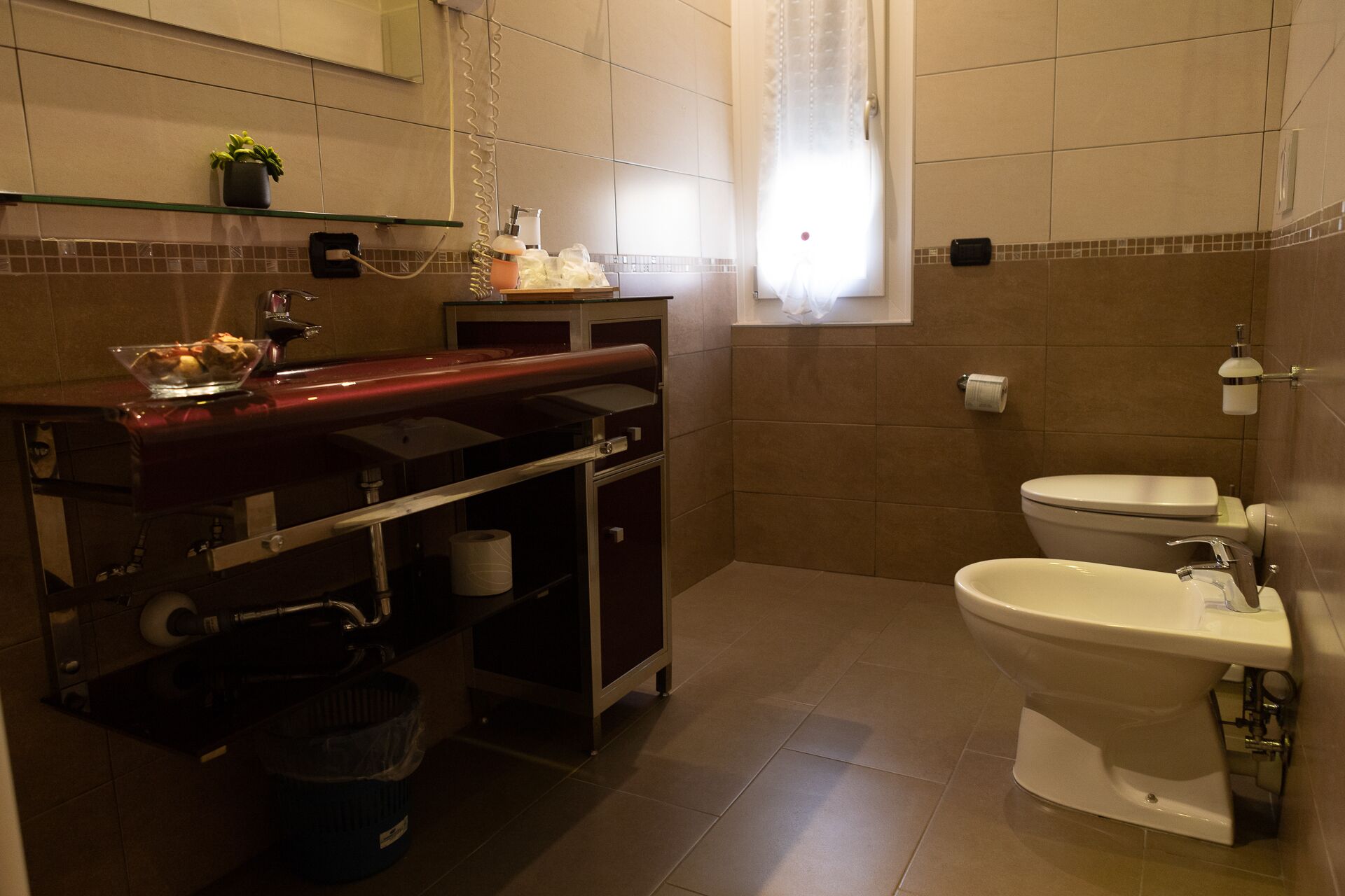 A bathroom with a toilet, bidet, sink, and a small shelf with toiletries.