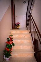 Una escalera con barandilla de madera, una planta en maceta con flores rojas y una pequeña mesa con un jarrón de flores en la parte superior.