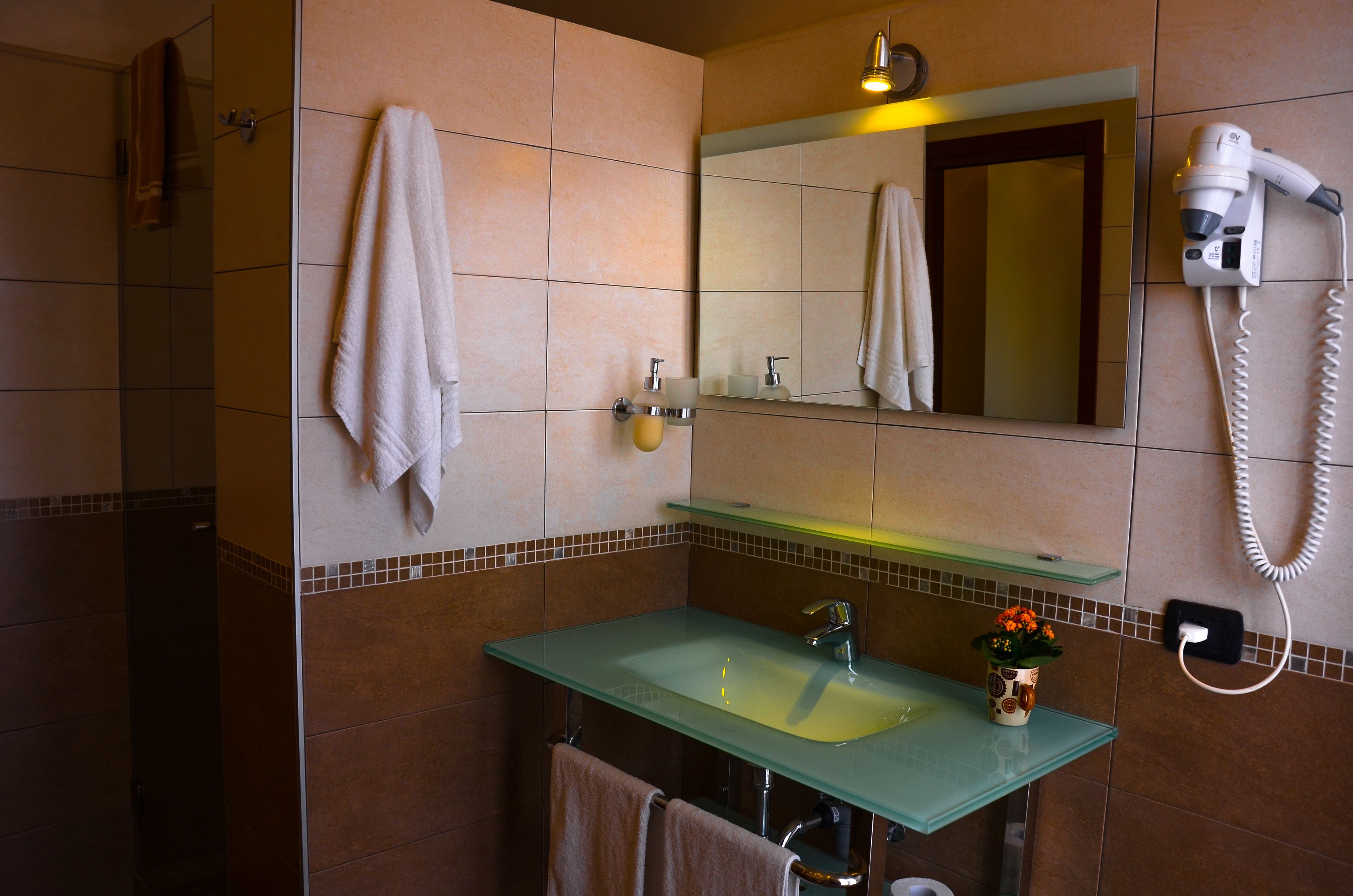 Ein Badezimmer mit einem Glaswaschbecken, einem Spiegel, einem Fön und zwei Handtüchern, die an der Wand hängen.